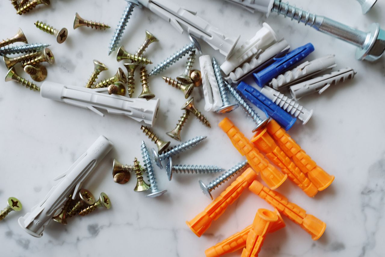 Set of various multicolored plastic dowels with assorted metal screws of different sizes placed on white marble table in modern workshop